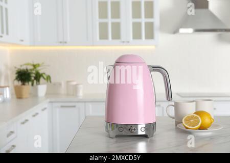 Modern electric kettle, cups and lemons on table in kitchen Stock Photo