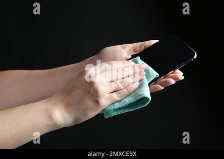 Woman cleaning smartphone with microfiber cloth against black background, closeup Stock Photo