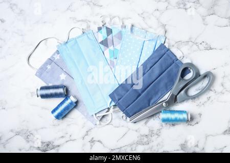 Homemade protective masks and sewing accessories on white marble background, flat lay Stock Photo