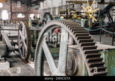 Detail of a gear of a vintage rolling mill. Blurred, old fashioned machines and industrial factory interior in the background. Stock Photo