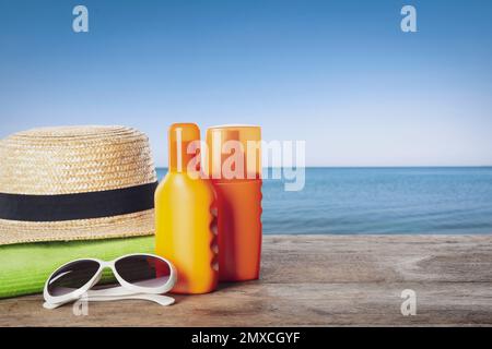 Set of sun protection products and stylish accessories on wooden table near sea. Space for text Stock Photo