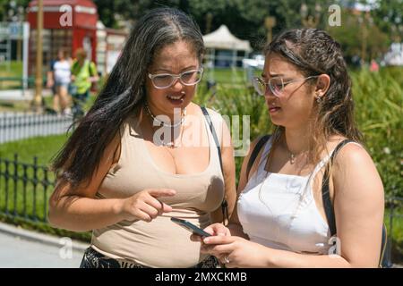 two young latin women tourists of venezuelan ethnicity, standing in a plaza lost looking at the map on the phone looking for the restaurant to go for Stock Photo