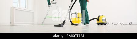 Professional young janitor using vacuum cleaner indoors, closeup view. Banner design Stock Photo