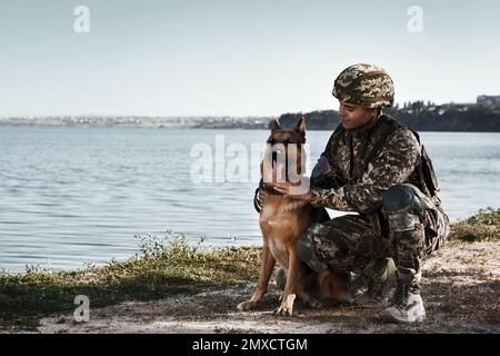Man in military uniform with German shepherd dog near river, space for text Stock Photo