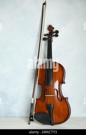 Beautiful violin and bow on white wooden table near light blue wall Stock Photo