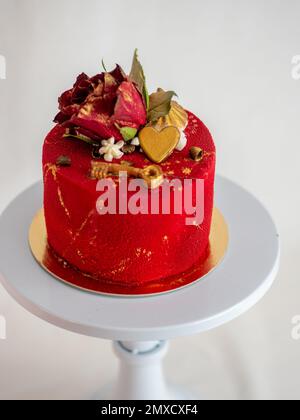 frosted red velvet cake with flower and heart toppers and golden paint strokes over white background studio shot Stock Photo