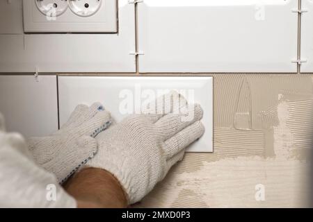 Male Worker Master Laying Ceramic Tiles on the Wall of Kitchen. Repairman Placing White Modern Tiles, Spreading Adhesive. Builder Installing Tile at R Stock Photo