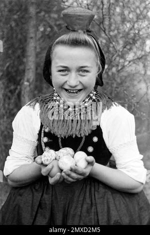 Junge Frau in Tracht mit gefundenen Ostereiern, Schwalm-Eder-Kreis in Hessen, 1938. Young woman in traditional costume with found Easter eggs, Schwalm-Eder region in Hesse, 1938. Stock Photo