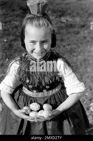 Mädchen in Tracht mit gefundenen Ostereiern, Schwalm-Eder-Kreis in Hessen, 1938. Girl in traditional costume with found Easter eggs, Schwalm-Eder region in Hesse, 1938. Stock Photo