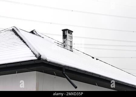 The roof of a single-family house is covered with snow against a cloudy sky, visible ceramic ventilation fireplace on the roof and falling snow. Stock Photo