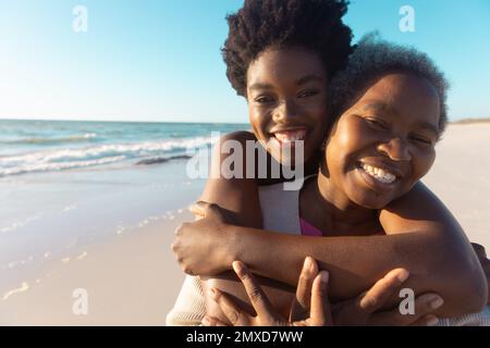 Portrait of african american loving young woman embracing senior mother at beach against sea and sky Stock Photo
