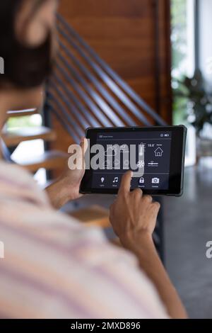 Vertical of hands of biracial man at home using tablet with smart home interface, copy space Stock Photo