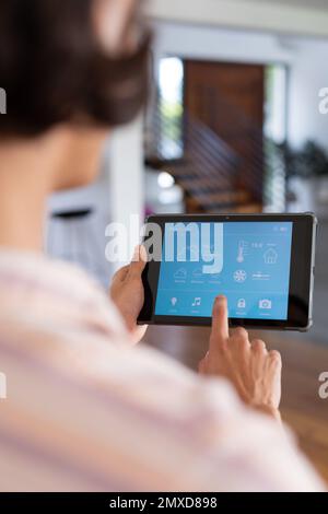 Vertical of hands of biracial man at home using tablet with smart home interface, copy space Stock Photo