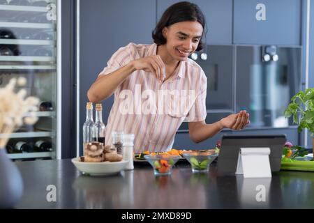 Happy biracial man cooking and using tablet in kitchen Stock Photo