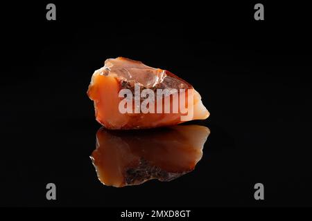 Reddish Carnelian Mineral Uncut Gem Stone on Black Background with Reflection Stock Photo