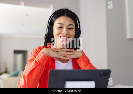 Image of biracial woman in headphones smiling during video call on tablet at home, copy space. Working from home, technology, communication and lifest Stock Photo