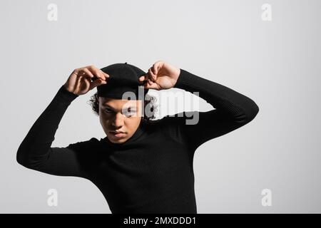 stylish african american man in black turtleneck touching beret and looking at camera isolated on grey,stock image Stock Photo