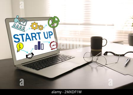 Modern laptop with word STARTUP and different icons on office table Stock Photo