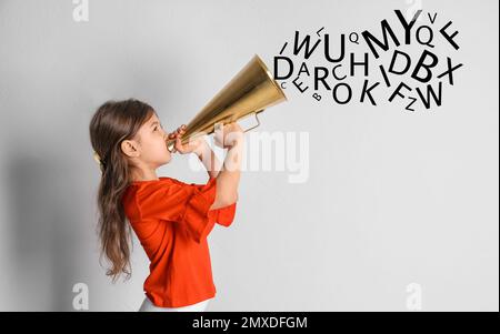 Adorable little girl with vintage megaphone and letters on light background. Speech therapy concept Stock Photo