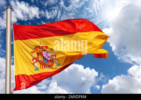 Spanish flag blowing in the wind against a blue sky with clouds, sunbeams and copy space. Spain Square (Plaza de Espana), Madrid, Spain, Europe. Stock Photo
