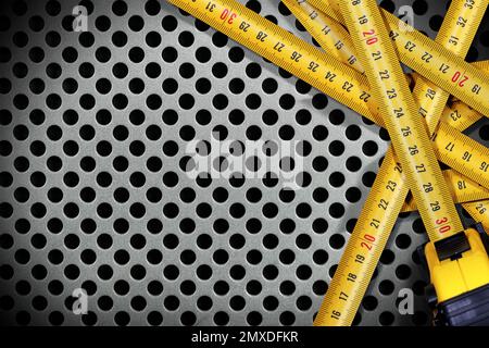 Group of yellow and orange tape measures on a silver metal background with many holes and copy space, photography. Stock Photo