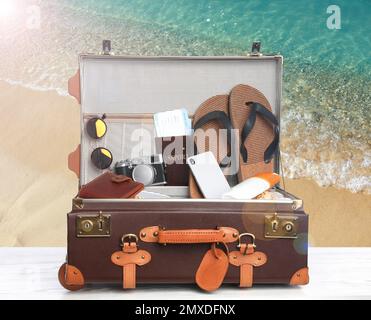 Suitcase with different beach objects on wooden table near sea Stock Photo