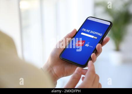 Woman holding smartphone with online shopping website on screen indoors, closeup Stock Photo