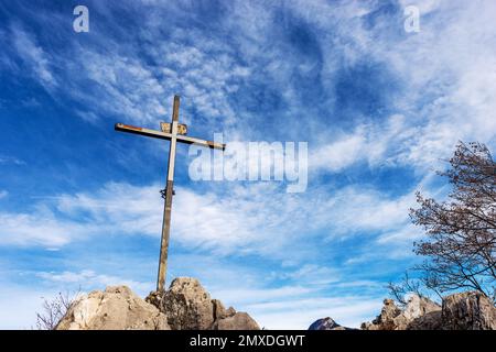 Metal religious cross on the top of a mountain peak against a blue sky with clouds and copy space. Monte Altissimo di Nago, Trentino Alto Adige, Italy Stock Photo