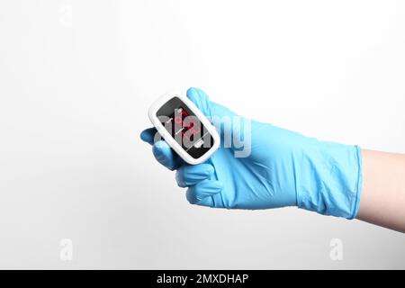 Doctor in gloves holding fingertip pulse oximeter on white background, closeup Stock Photo