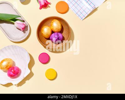 Flat lay still life with colored easter eggs and pink tulips on bright yellow sunlit background. Stock Photo