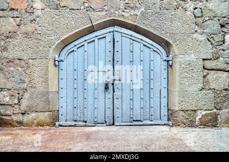 Blue wooden gate on wall surrounded by stones in medieval design hide mysterious things from arriving visitors. Exterior of medieval place Stock Photo