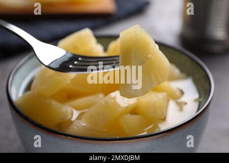 Fork with canned pineapple piece over bowl on table, closeup Stock Photo