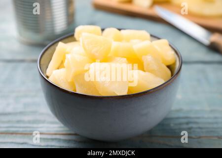 Pieces of delicious canned pineapple in bowl on light blue wooden table, closeup Stock Photo