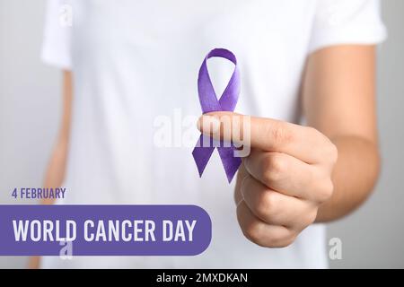 Woman holding purple ribbon against grey background, closeup. World Cancer Day Stock Photo