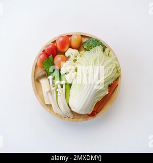 top view flat lay mix fresh vegetable with chinese cabbage,mushroom,tomato,carrot,green peas,cucumber,broccoli on wood round plate white background.id Stock Photo