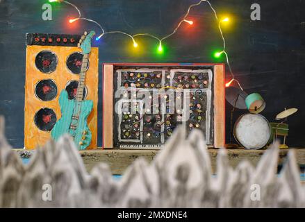 Grungy cardboard models of synthesizer,drum kit,guitar,amplifier on stage and blurred generic audience in the foreground.Music festival summer season, Stock Photo