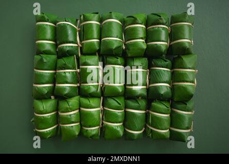 top view thai tradition sweet dessert made with bean coconut milk sticky rice wrap by fresh banana leaf nature green cute package bamboo bundle on dar Stock Photo