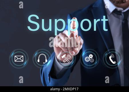 Man pointing at icon on virtual screen against dark background, closeup. Technical support service Stock Photo