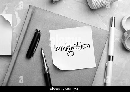 Note with word IMMIGRATION and stationery on grey table, flat lay Stock Photo