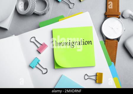 Note with word IMMIGRATION and stationery on grey grey table, flat lay Stock Photo