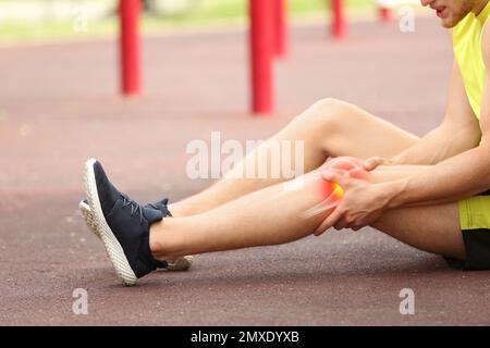 Young man suffering from knee pain on sports ground, closeup Stock Photo