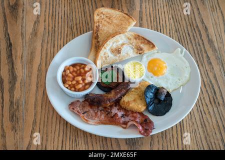 Full english fried breakfast served on a white plate on a cafe table - point of view Stock Photo