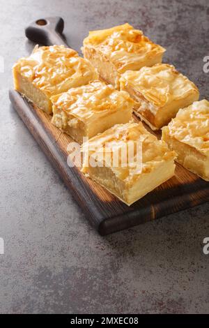Galaktoboureko is a traditional Greek dessert featuring a custard in a crispy phyllo pastry closeup on the wooden board on the table. Vertical Stock Photo