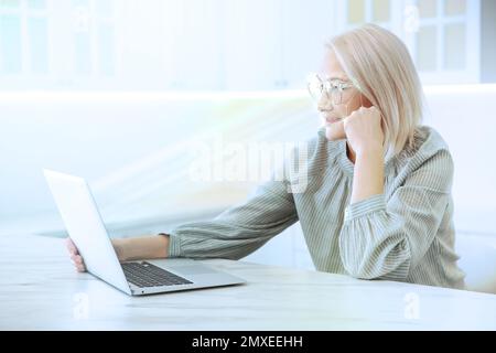 Facial recognition system. Mature woman using laptop in kitchen Stock Photo