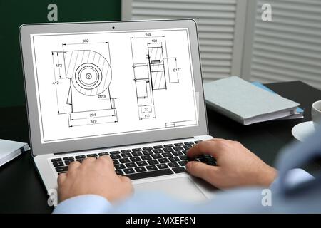 Male engineer working with technical drawing on laptop indoors, closeup Stock Photo