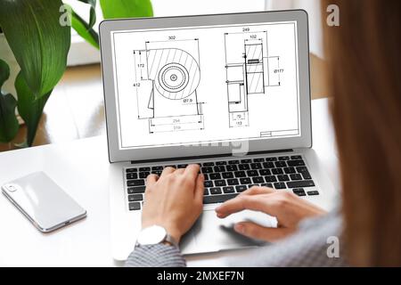 Female engineer working with technical drawing on laptop indoors, closeup Stock Photo