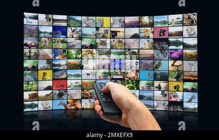 Streaming video services. Man using remote control to change channels on TV Stock Photo