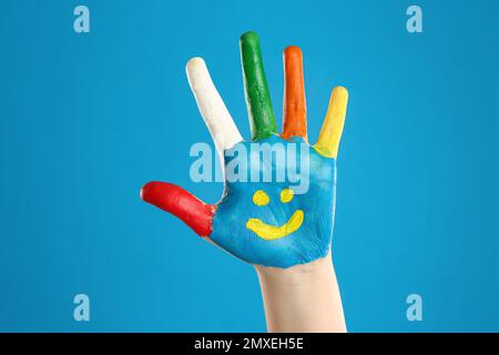 Kid with smiling face drawn on palm against blue background, closeup Stock Photo