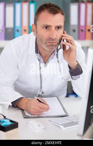 male doctor using telephone while working on computer Stock Photo