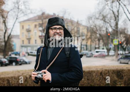 A senior tourist takes pictures of the winter city on his film camera. Travel and hobby concept. Stock Photo